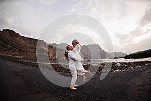 Male groom holding on hands female bride on the beach