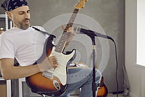 Male guitarist playing riff on his electric guitar in modern studio with microphone