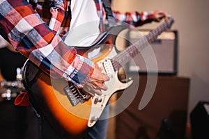 a male guitarist strums the strings of an electric guitar while tuning before being used photo