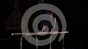 Male gymnast acrobat performs handstand on parallel bars in a dark room in slow motion
