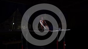 Male gymnast acrobat performs handstand on parallel bars in a dark room in slow motion