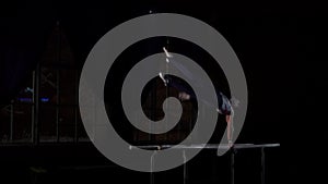 Male gymnast acrobat performs handstand on parallel bars in a dark room in slow motion sharing flips and landing on the