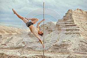 Male gymnast does tricks on a pylon.