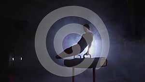Male gymnast performs Pommel horse exercise in a dark room in smoke in slow motion. Sports for health and achievement