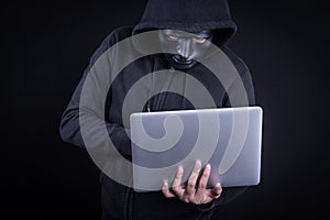 Male hacker with black mask carrying laptop