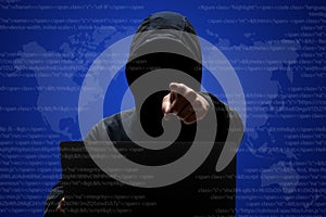 Male hacker with dark face in hoodie, stands in front of laptop computer, points at camera, steals data, downloads private informa photo