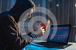 Male hacker in the hood holding the phone in his hands trying to steal access databases. Concept of cybersecurity