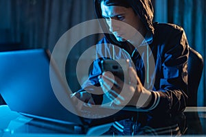 Male hacker in the hood holding the phone in his hands trying to steal access databases with passwords. Cybersecurity