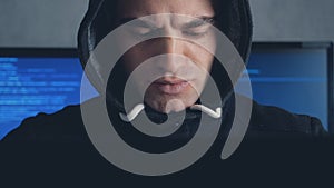 Male hacker in hood working on a computer in a dark office room. Shot on steadicam
