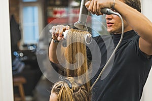 Male hairdresser blowdrying long hair of a woman