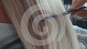 Male hairdresser combing hair to blonde girl in beauty salon, close-up