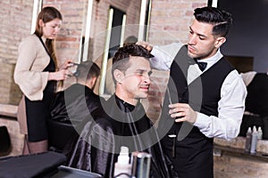 Male hairdresser cutting hair of male client