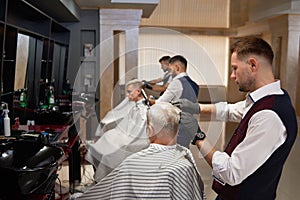 Male hairdressers grooming client`s haircuts in barbershop.