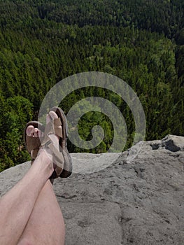 Male hairy legs with sandals rest on rocky summit above valley