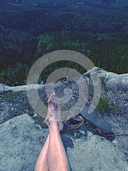 Male hairy legs with sandals rest on rocky summit above valley