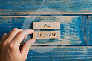 Male hand assembling a We apologize sign written on two wooden pegs