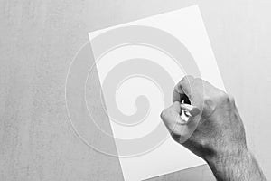 Male hand with a ballpoint pen and a blank white sheet of paper on grey background, top view closeup