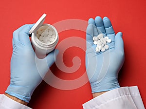 Male hand in a blue sterile rubber glove holds a stack of pills on a red background