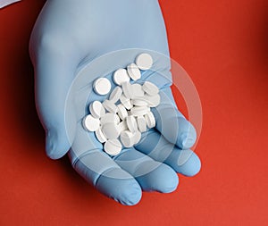 Male hand in a blue sterile rubber glove holds a stack of pills on a red background