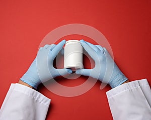 Male hand in a blue sterile rubber glove holds a stack of pills on a red background