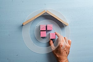 Male hand building a house of pink wooden blocks