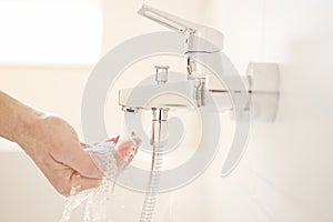 Male hand checking the temperature of flowing water from a faucet in a bright bathroom