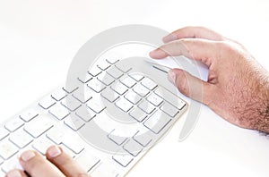Male hand clicking on a mouse and typing on a white keyboard on a white table