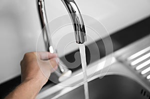 Male hand and close up on modern kitchen metal faucet and metal kitchen sink with a running water.