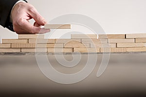 Male hand completing building wall of wooden bricks