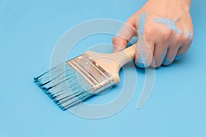 Male hand covered in paint, holding a paint brush on a wooden background surface