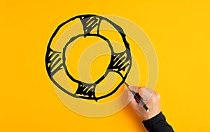 Male hand drawing a lifesaver or lifebuoy sketch on yellow background. Insurance, safety, assistance or aid in business