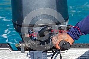Male hand driving a inflatable boat holding the tiller of an outboard motorboat.