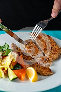 Male hand eating from big dish German schnitzel with salad