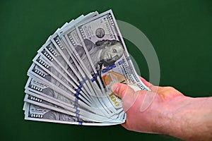 male hand with a fan of dollars on a green background