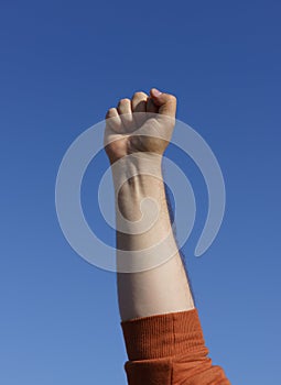 Male hand in a fist raised in the blue sky