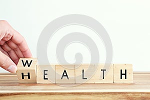 Male hand flipping wooden cubes with the text wealth â€“ health. Wellness and insurance concept