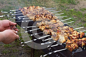 The male hand flips the finished pork skewers on skewers. Cooking meat on a fire in nature