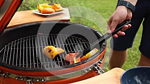 Male hand frying fresh juicy sweet pepper slice on barbecue turning vegetables using forceps