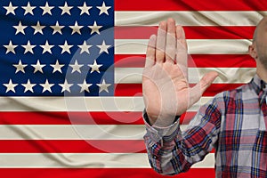 Male hand with a gesture of protest, oaths against the backdrop of the US silk national flag, concept of denial and prohibition