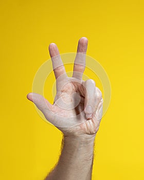 Male hand gesture showing three fingers on yellow background.