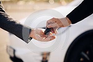 Male hand gives a car keys to male hand in the car dealership close up. Unrecognized auto seller and a man who bought a