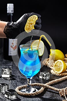 Male hand in glove squeezing lemon into glass with Blue Lagoon cocktail photo