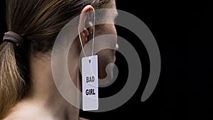 Male hand hanging bad girl label on female ear, social disrespect and submission