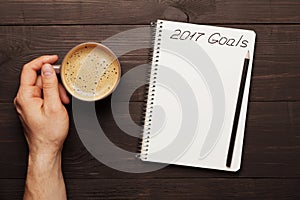 Male hand hold cup of coffee and notebook with goals for 2017. Planning and motivation for the new year concept. Top view.