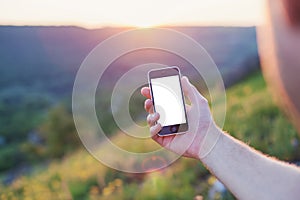 Male hand hold the phone on a background of sunset