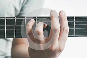 Male hand holding a barre chord on the acoustic guitar, close-up