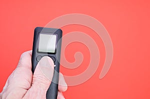 Male hand holding a black remote controller on red background