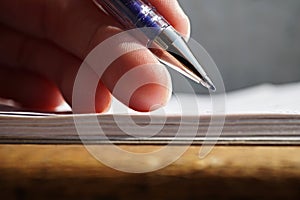 Male hand holding a blue office pen and writing to the white lined notepad as a symbol of taking notes or business communication