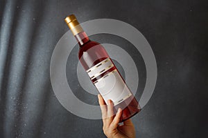 Male hand holding bottle of pink red wine, natural fruit alcohol liquor with empty label on grey background. Mock up, template for