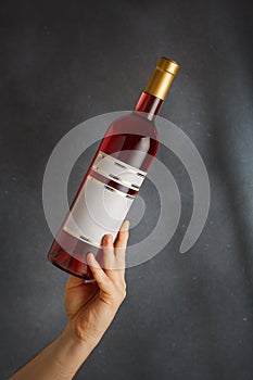 Male hand holding bottle of pink red wine, natural fruit alcohol liquor with empty label on grey background. Mock up, template for